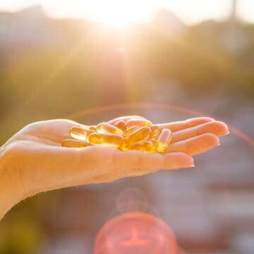 Hand of a woman holding fish oil Omega-3 capsules, urban sunset background. Healthy eating, medicine, health care, food supplements and people concept Ендокринологи змінюють правила: чи потрібно пити вітамін D влітку?